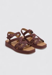 Sandales tressées marron avec une semelle plate, des sangles ajustables et un dessus texturé. Comprend une semelle intérieure rembourrée pour le confort.