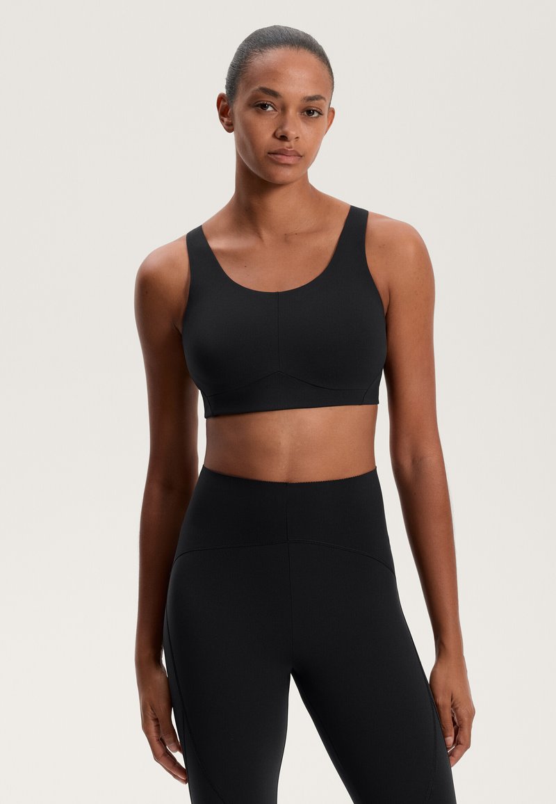 Črna športna modrček z širokimi naramnicami in gladko teksturo, ki ima brezšivno zasnovo in subtilno ukrivljen sprednji šiv.