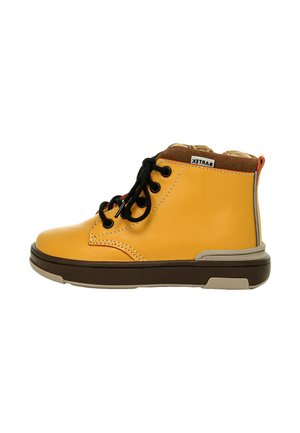 Zapato casual de caña alta amarillo con cordones negros, cuello acolchado marrón, suela beige y marrón oscuro, y una pequeña etiqueta de tela en el lateral.