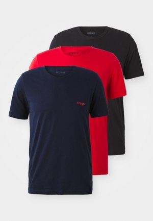Trois t-shirts unis à col rond à manches courtes de la marque HUGO en bleu marine, rouge et noir, superposés l'un devant l'autre sur un fond blanc.