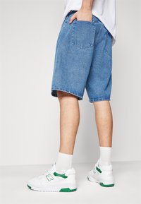 Denim shorts in light blue with a relaxed fit. Features side and back pockets. Paired with white sneakers with green accents.