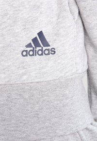 Gros plan sur un tissu gris avec le logo Adidas bleu foncé imprimé sur la zone poitrine d'un sweat-shirt.