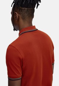 Polo-shirt met korte mouwen in gebrand oranje, met een textuurstof, een kraag met blauwe en groene gestreepte accenten, en een getailleerde pasvorm.