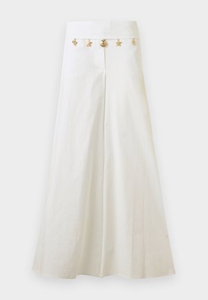 Λευκά παντελόνια με φαρδύ πόδι και ψηλή μέση με χρυσά, θαλασσινής θεματολογίας, διακοσμητικά κρεμασμένα στη μέση, όπως αστερίες και κοχύλια.