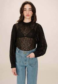 Zwarte kanten langemouwen top met een hoge hals, doorschijnende stof en pofmouwen, gecombineerd met lichtblauwe high-waisted jeans.