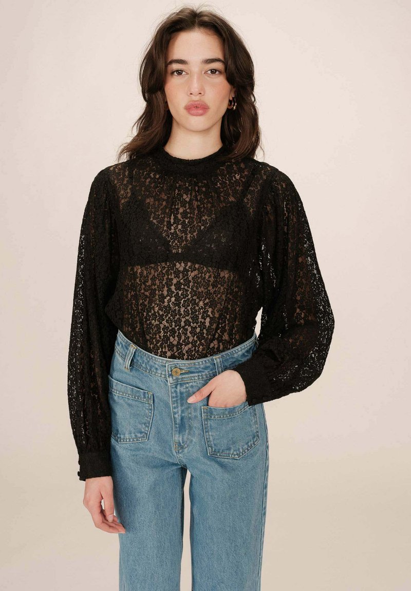 Zwarte kanten langemouwen top met een hoge hals, doorschijnende stof en pofmouwen, gecombineerd met lichtblauwe high-waisted jeans.