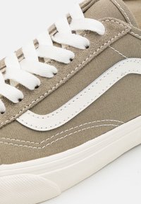 Beige plátěné tenisky s bílým šitím a tkaničkami, s bílým koženým detailem ve tvaru swoosh podél boku a texturovanou gumovou podešví.