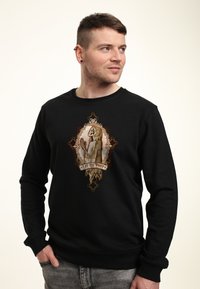 Felpa nera con una grafica centrale che presenta uno scheletro in un mantello con cappuccio, affiancato da dettagli dorati ornamentali e dalla frase "Let Us Pray".