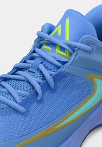 Gros plan d’une chaussure de sport bleue avec tissu en mesh, lacets bleu clair, logo vert néon sur la languette et motif swoosh turquoise et or sur le côté.