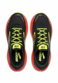 Zapatillas de correr negras con parte superior de malla texturizada, cordones verde neón y suela roja brillante. Marca "Brooks" en el talón y la lengüeta.