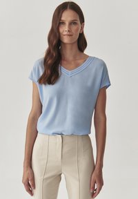 Top leggero blu chiaro a maniche corte con scollatura a V, caratterizzato da una cucitura decorativa lungo il collo; tessuto morbido e vestibilità comoda.