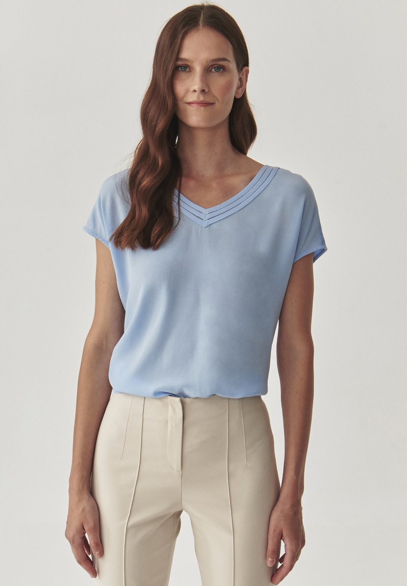 Top leggero blu chiaro a maniche corte con scollatura a V, caratterizzato da una cucitura decorativa lungo il collo; tessuto morbido e vestibilità comoda.