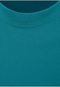 Tessuto di cotone verde acqua di una maglietta che mostra una texture liscia con un collo rotondo e cuciture visibili lungo il colletto.