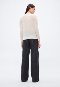 Bluză bej deschis cu mâneci lungi, confecționată dintr-un material transparent, asortată cu pantaloni denim largi, de culoare închisă. Tiv simplu cu striații.