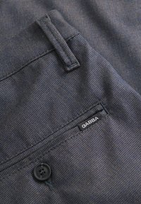 Țesătură texturată de culoare albastru închis, cu un buton vizibil și o etichetă neagră cu inscripția "GABBA". Designul include o buzunar cu un detaliu cusut.