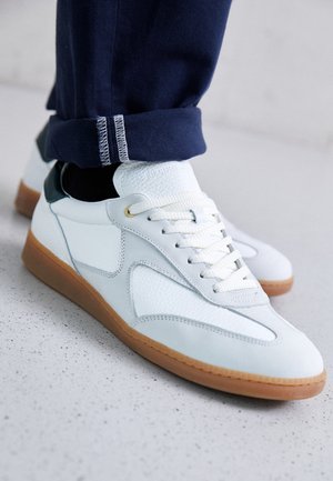 White leather sneakers with textured overlays, a light blue accent, and a gum rubber sole. Laces are white; stitching is visible at the cuff.