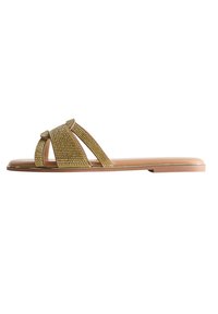 Sandales plates avec une bride ornée de strass dorés, un design ouvert à l'avant et une semelle synthétique beige. Texture lisse et forme minimaliste.