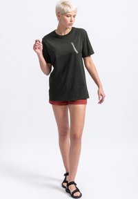 Zwart katoenen t-shirt met een ontwerp met korte mouwen, voorzien van een subtiele grafiek van een arm op de voorkant. Gecombineerd met rode shorts en zwarte sandalen.