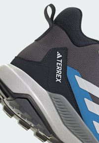 Υπαίθριο παπούτσι Terrex με γκρι επάνω μέρος από πλέγμα, μπλε και λευκές λεπτομέρειες, λαστιχένια σόλα και υφασμένη φτέρνα για καλύτερη πρόσφυση.