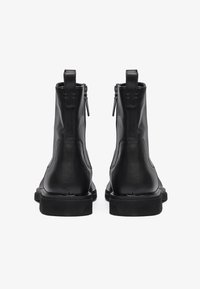 Botas negras de cuero hasta el tobillo con un acabado suave, cremalleras laterales y tiradores, que presentan una suela robusta y un diseño minimalista.