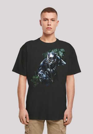 Sort bomulds t-shirt med grafik af en karakter i sort jakkesæt med sølvnuancer og kløer, omgivet af en grøn baggrund.