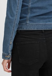 Chaqueta de mezclilla en azul claro con puños abotonados, combinada con jeans ajustados negros que presentan dos bolsillos traseros y una textura suave.