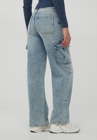 Jasnoniebieskie dżinsowe spodnie cargo o luźnym kroju, z kieszeniami bocznymi, kontrastowymi szwami i postrzępionymi wykończeniami.