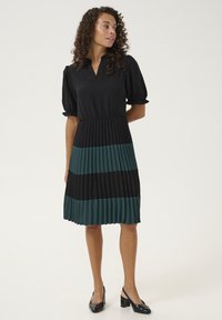 Čierne a tyrkysové plisované šaty s výstrihom do V, krátkymi nadýchanými rukávmi a elastickým pásom. Hladká tkanina a kontrastný horizontálny pruhový dizajn.