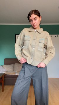 Chaqueta caqui abotonada con dos bolsillos en el pecho y cuello solapa, combinada con pantalones grises de pierna ancha; detalles de costura visibles.