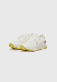 Chaussures de sport blanches avec une tige en mesh texturée, semelle extérieure en caoutchouc jaune, accent au talon gris contrastant et fermeture à lacets traditionnelle.