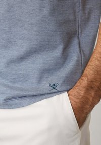 Světle modré pruhované tričko s krátkým rukávem, vyrobené z bavlny, s dekorativním vyšívaným detailem na lemu a uvolněným střihem.