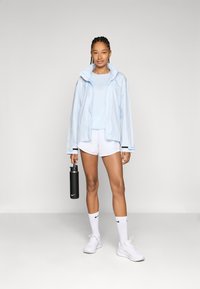 Chaqueta de lluvia azul claro, pantalones cortos blancos, zapatillas blancas y botella de agua negra. Presenta una capucha y acentos negros contrastantes en las mangas.