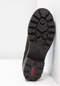 La semelle de chaussure noire présente un design en caoutchouc texturé avec des crampons profonds pour une meilleure adhérence. On remarque la marque rouge "rieker" ainsi que l'indication de taille 37.