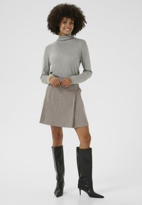 Grauer Rollkragenpullover, karierter Minirock in Braun und Creme, schwarze kniehohe Stiletto-Stiefel. Glatte Texturen und enganliegendes Design.