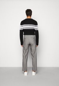 Musta neulepaita, jossa valkoisia ja harmaita vaakaraitoja. Yhdistetty harmaisiin pikkutaskupukuisiin housuihin ja valkoisiin tennareihin.