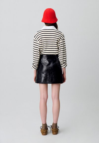 Camisa de rayas de manga larga en crema y negro, falda mini de cuero negra, sombrero de cubo de lana roja, zapatos de cordones marrones y calcetines marrones.