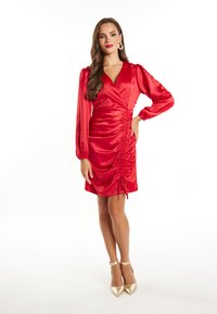 Rochie roșie din satin, cu mâneci lungi tip puff, decolteu în V și detalii plisate pe lateral. Asortată cu pantofi cu toc înalt aurii. Textură netedă.
