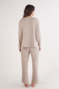 Beige loungewear-set bestaande uit een loszittend shirt met lange mouwen en bijpassende broek, gemaakt van zachte stof met een gladde textuur en een ontspannen silhouet.