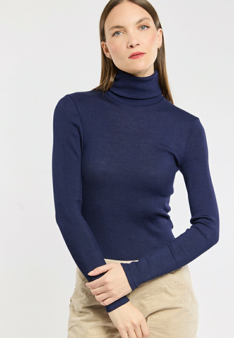 Pull à col roulé bleu marine en texture côtelée, avec des manches longues et une coupe ajustée, associé à un pantalon beige.