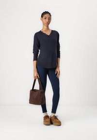 Pull marin à col en V avec des détails en dentelle, associé à un jean slim bleu foncé, un sac en suède marron et des chaussures à plateforme beiges.