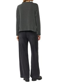 Sweter w czarno-białą kratę z długimi rękawami i okrągłym dekoltem; w połączeniu z eleganckimi, szerokimi spodniami w kolorze ciemnoszarym i wysokim stanem oraz masywnymi czarnymi butami.