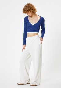 Blauw, cropped shirt met lange mouwen en knoopdetails, gecombineerd met witte, wijde broek. Heeft een ontspannen pasvorm en een soepele stof.