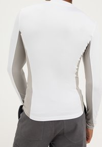 Langärmeliger Rashguard mit einem weißen Oberteil und grauen Seitenpaneelen. Glattes, dehnbares Material, das für Wasseraktivitäten konzipiert ist.