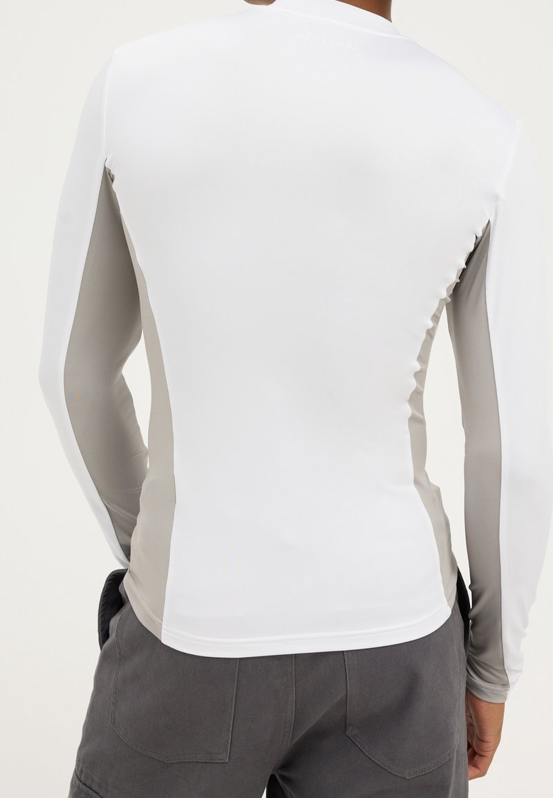 Rash guard s dlouhým rukávem s bílým tělem a šedými bočními panely. Hladká, elastická tkanina navržená pro vodní aktivity.