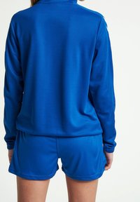 Modrý sportovní teplákový komplet s dlouhými rukávy a šortkami. Hladká, elastická tkanina; minimalistický design; s bílými akcenty na ramenou.