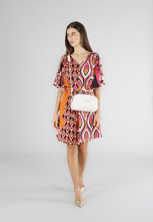 Abito A-line colorato con scollo a V, maniche corte e un audace motivo geometrico in rosa, arancio e nero; abbinato a una borsa a tracolla bianca.