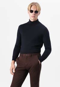 Tengerés turtleneck pulóver puha kötött anyagból, barna szabott nadrággal párosítva. Az öltözék illeszkedő ujjakból és egyenes sziluettből áll.
