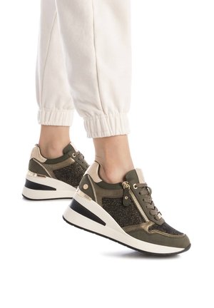 Zapatillas deportivas verdes y doradas con un panel texturizado brillante, punta redondeada y suela blanca elevada, que cuenta con un zipper lateral y cordones.