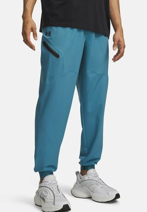 Turquoise sportbroek met elastische boorden, ritszak aan de zijkant en een gladde textuur, gecombineerd met witte sneakers met zwarte accenten.