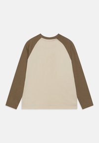 Långärmad T-shirt med en krämfärgad kropp och bruna raglanärmar. Tillverkad av bomull, rund hals och en enkel, ren design.